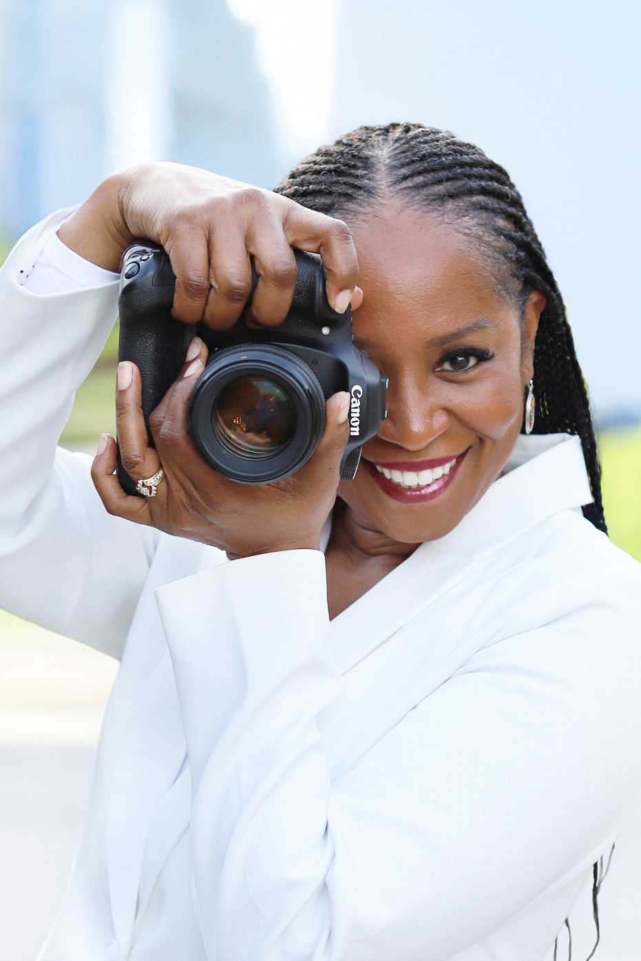 Lady photographer wearing a white suit and a big smile, holding her camera.